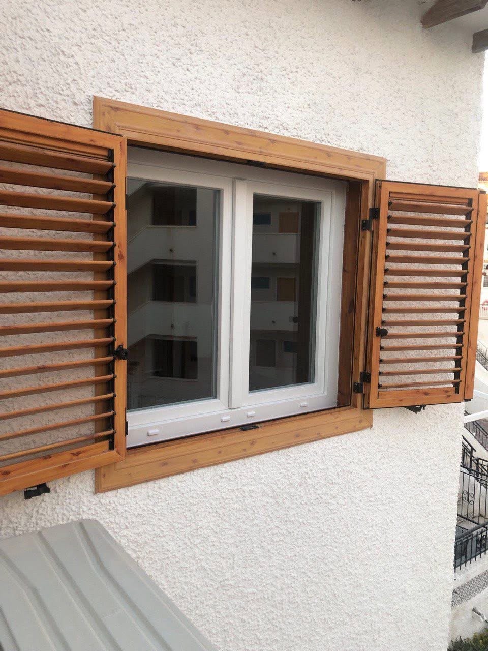 Ventana blanca de dos hojas junto a contraventanas de madera abiertas